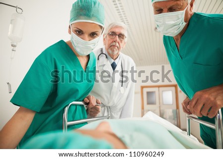 Doctors looking at a patient while leaning on a bed in hospital corridor