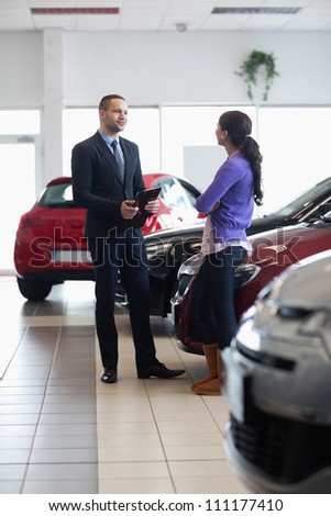 Salesman and a woman talking next to a car in a car shop