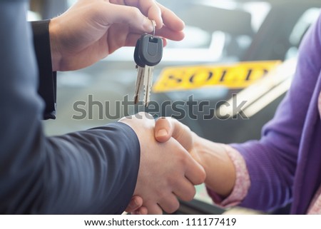 Person shaking hands in front of a sold car in a car shop
