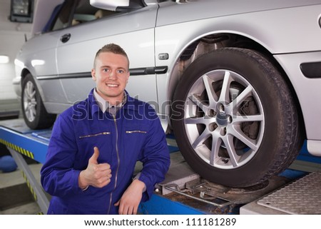 Man looking at camera next to a car with his thumb up in a garage