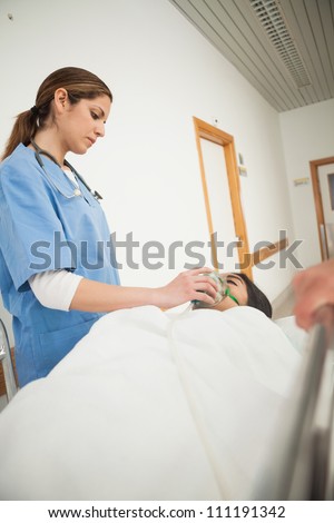 Nurse putting oxygen mask on a female patient in hospital corridor