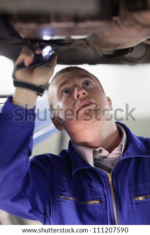 Mechanic illuminating the below of a car with a flashlight in a garage