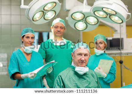 Smiling surgeon sitting with a team behind him in a surgical room