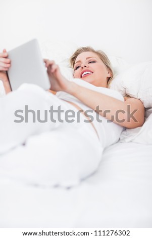Blonde smiling while using an book reader while lying on her bed