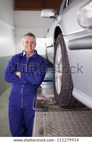 Front view of a mechanic smiling next to a car in a garage