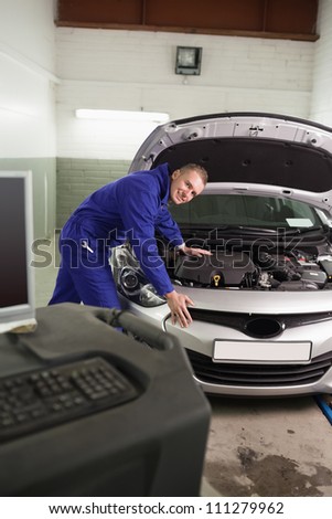 Smiling mechanic leaning on a car next to a computer in a garage