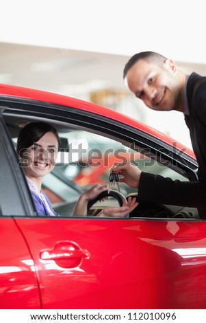 Happy salesman giving car keys to a woman in a car shop