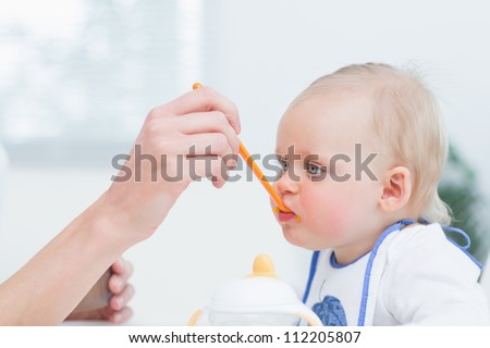 Baby with a plastic spoon on his mouth in living room