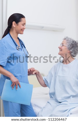 Elderly patient holding the hand of a nurse in hospital ward