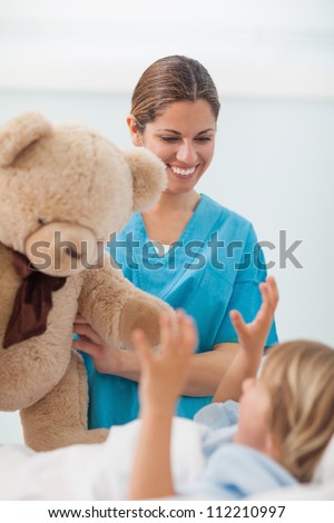 Smiling nurse showing a teddy bear to a child in hospital ward