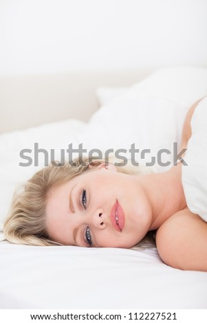 Pretty woman lying under a white duvet on her bed