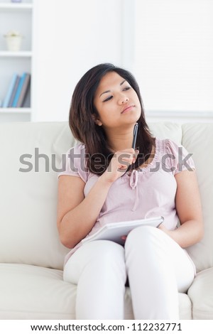 Woman thinking while sitting on a couch and holding a pen and a notebook in a living room