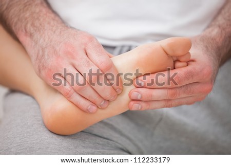 Podiatrist massaging the foot of a woman while holding it on his thigh indoors