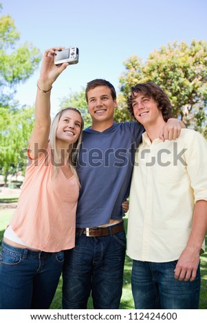 Three smiling friends taking a pictures of themselves in a park