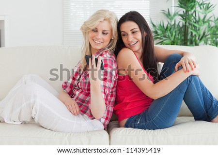 Women sitting back to back on the couch showing phones while smiling