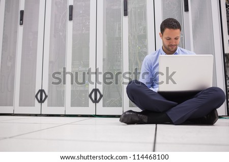 Technician sitting on floor working on laptop in data center
