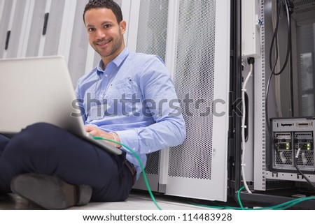 Happy technician working on laptop connected to server in data center