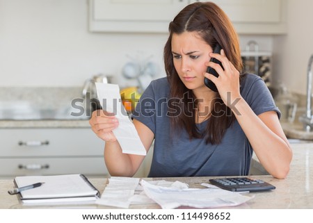 Woman calling while calculating bills in kitchen