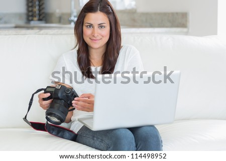 Brunette holding laptop and camera while smiling