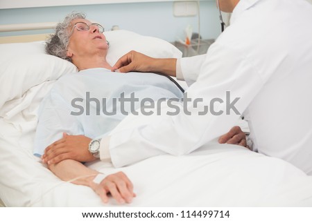 Doctor listening to heartbeat of elderly female patient in hospital bed