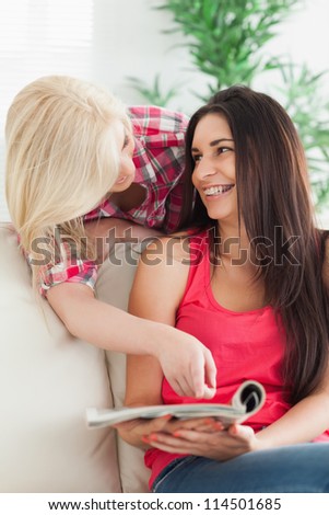 Woman pointing at magazine to friend on couch and smiling