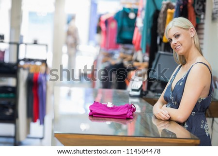 Woman smiling behind counter with folded clothes in clothing store