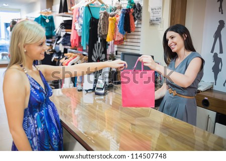Woman handing over shopping bag at chas register in clothes store