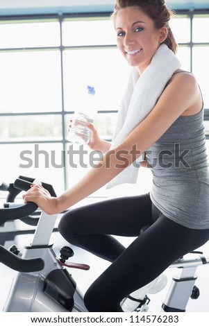 Woman riding an exercise bike and drinking a bottle of water