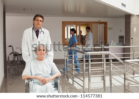 Old woman sitting in a wheelchair while the doctor is pushing in hospital corridor