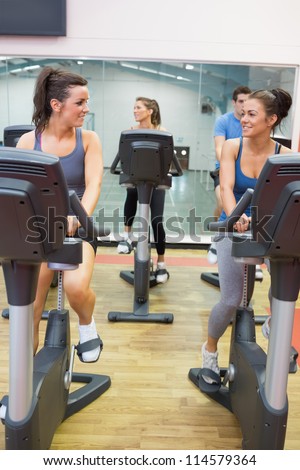 Women talking while training on exercise bike in gym