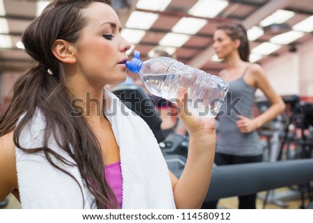 Woman drinking bottle of water in the gym during exercise