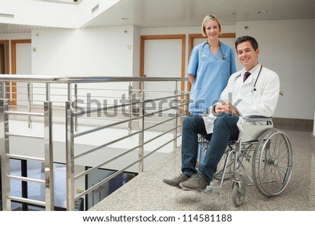 Nurse standing with doctor sitting in wheelchair in hospital corridor
