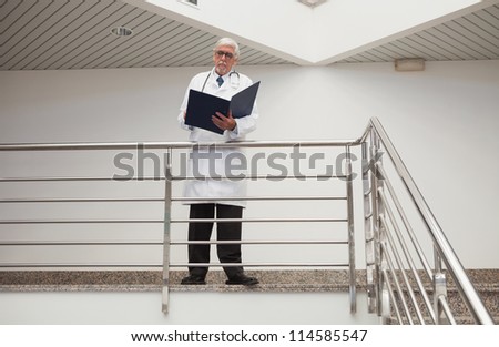 Doctor reading patient files leaning against railing in hospital corridor