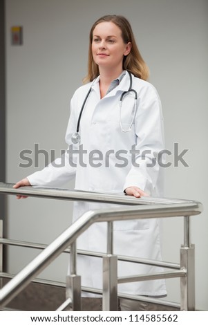 Female doctor proudly standing on the top of the stairs in hospital corridor