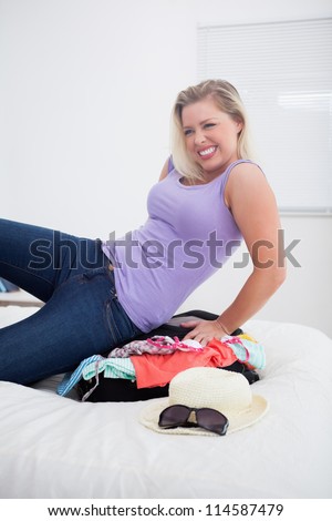 Blonde trying hard to close her luggage in her bed