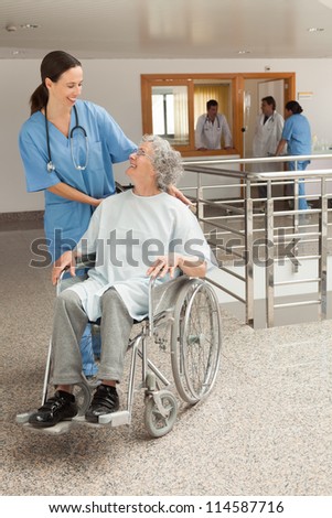 Nurse smiling at old women sitting in wheelchair in hospital corridor