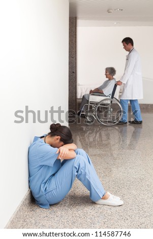Nurse sitting on the ground in the hallway of the hospital with head in hands