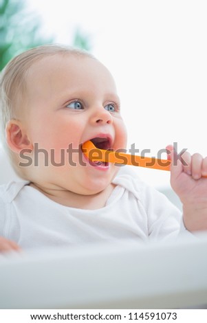 Baby holding a plastic spoon in his mouth in living room