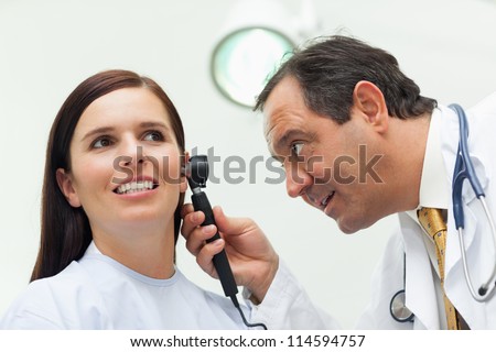 Doctor using an otoscope to look at the ear of his patient in an examination room