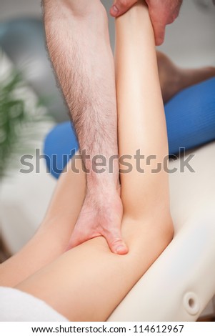 Doctor extending the leg of his patient while holding his ankle and his knee indoors