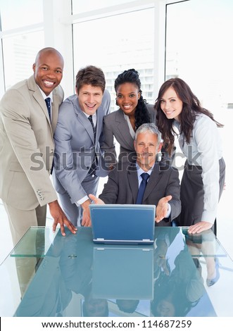 Young business people standing behind their director proudly showing the laptop