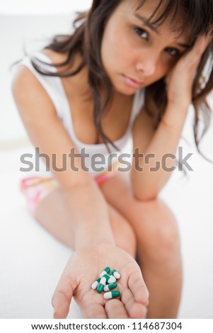 Sad student holding a lot of medicine while sitting on her bed