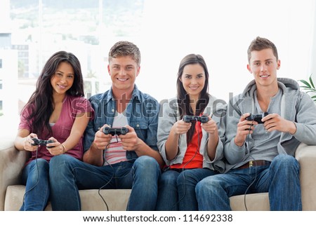A smiling group of friends sit on the couch with controllers playing a game together