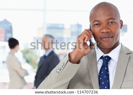 Young serious executive in a suit talking on the phone while his team stands behind him