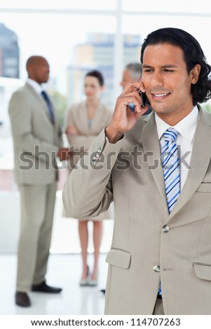 Businessman using a mobile phone while his team are communicating behind him