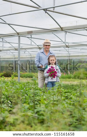 Man standing with granddaughter holding purple flowers in greenhouse