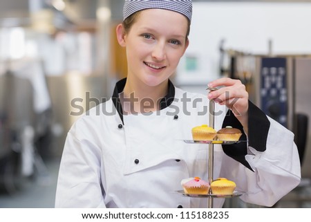 Happy chef holding tiered cake tray of cupcakes in kitchen
