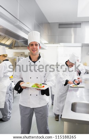 Happy chef holding a salmon dish in busy kitchen