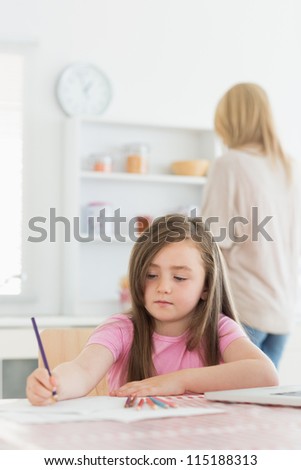 Girl sitting at the table drawing a picture in kitchen with mother in background