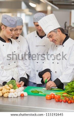 Chef teaching cutting vegetables to three trainees in the kitchen
